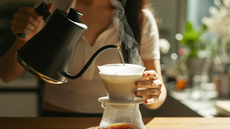 Mani che versano acqua calda da un bollitore a collo d'oca su un dripper