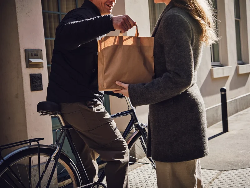 Fattorino in bicicletta consegna un sacchetto di carta a una porta di Milano